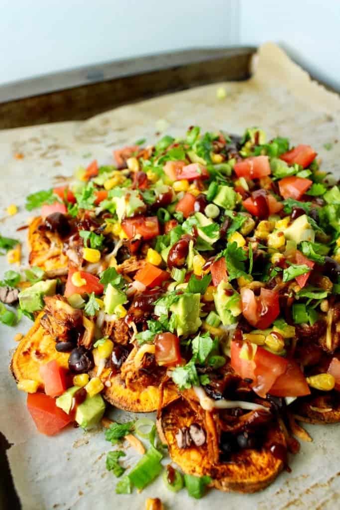 Loaded BBQ Chicken Sweet Potato Nachos piled high with chopped veggies, avocado, and cilantro on parchment paper