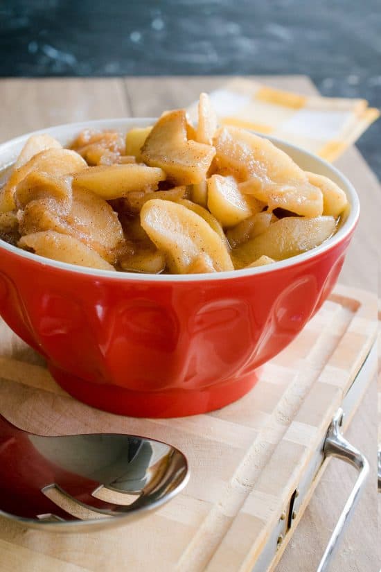 Red Bowl of fried apples with a spoon by the side.