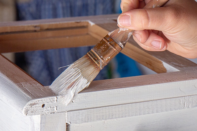Painting a dresser white with a paintbrush.