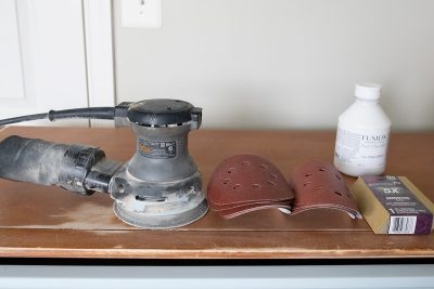 tools for painting furniture including orbital sander, sanding pads and blocks, and adhesive primer