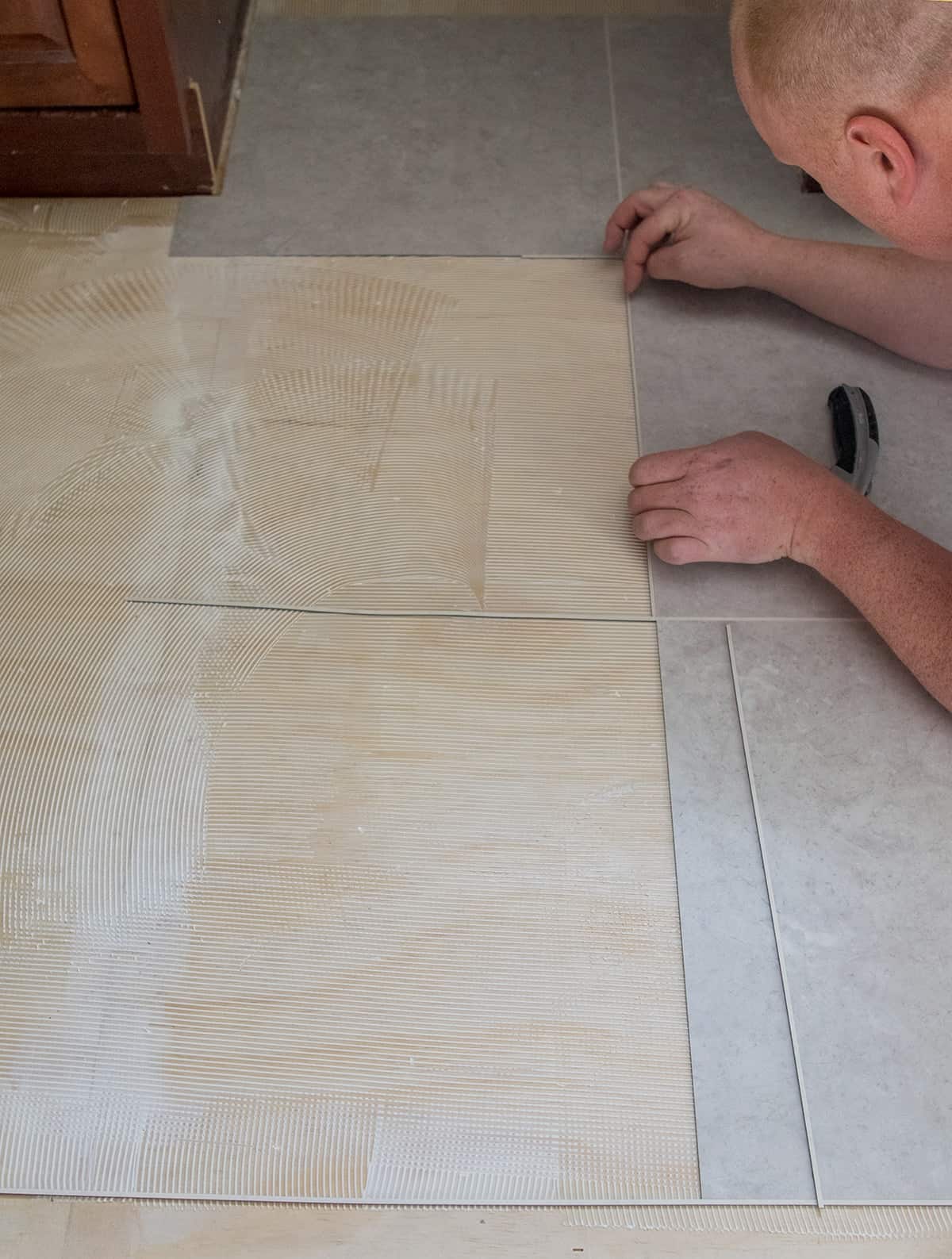 Man installing luxury vinyl tile on a kitchen floor including grout strips.