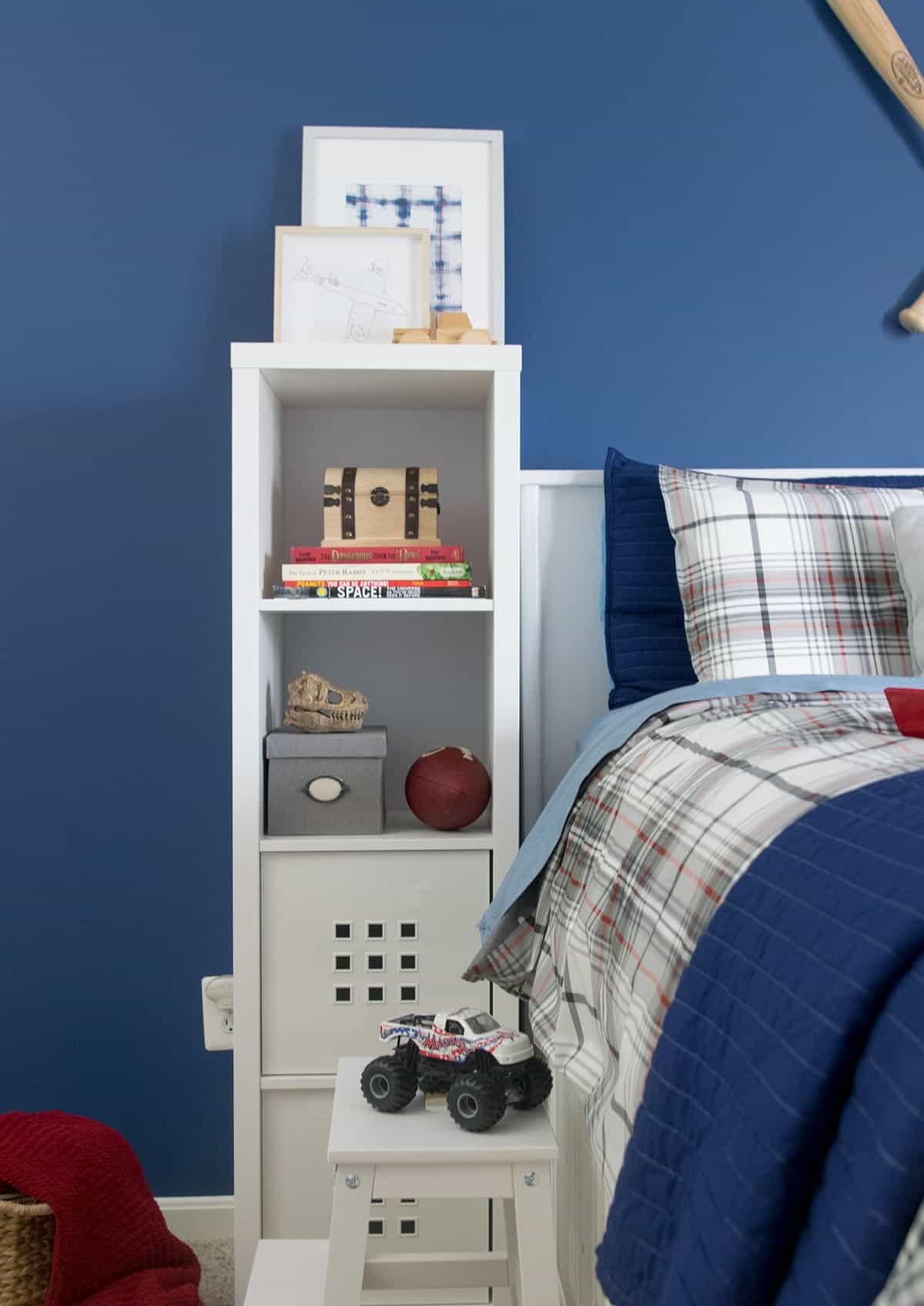 White bedside bookshelf next to captain's bed with blue walls and sports decor. 