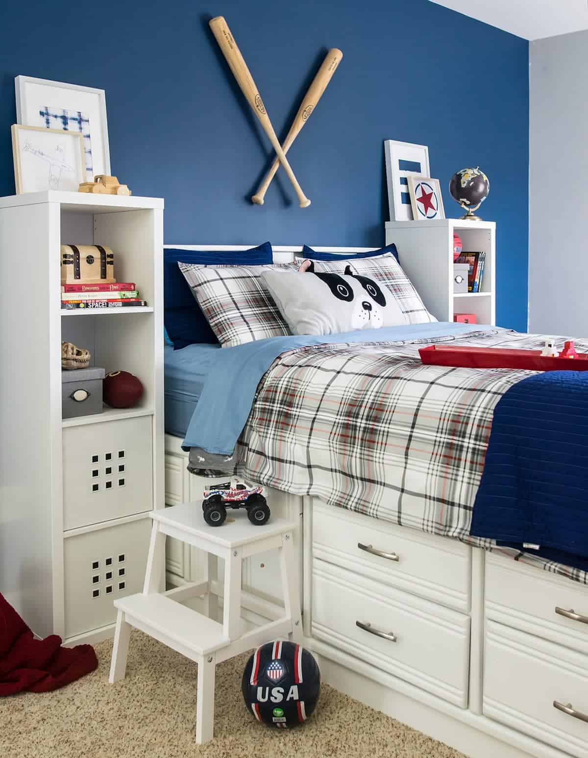 Boy's room after makeover with refinished white captain's bed and step stool with plaid bedding, white lockers, and various sports related decor. 