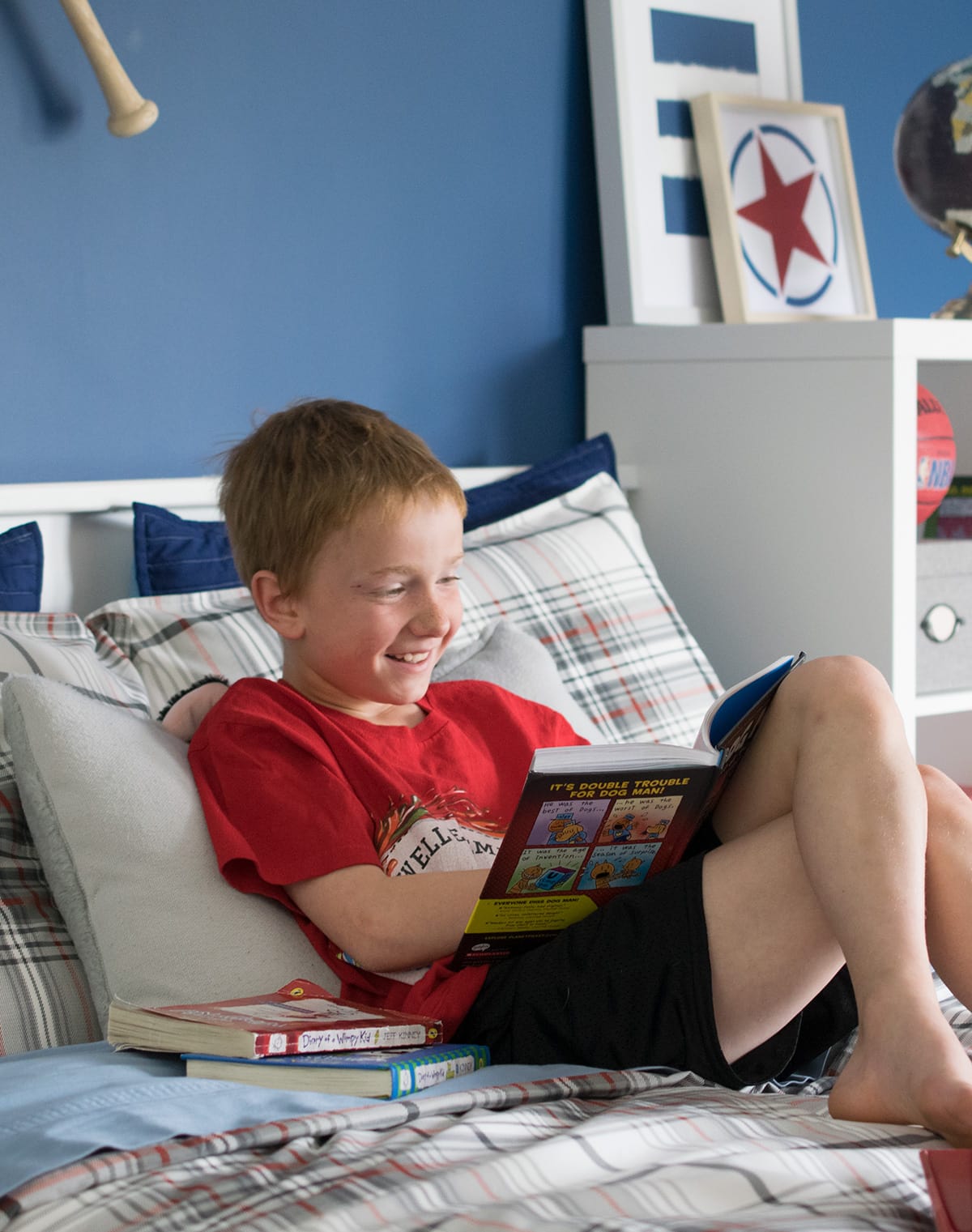 Boy reading a book on his newly refinished captain's bed with plaid bed coverings. 