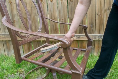 Woman using a wire brush to remove chipping paint from metal chair.