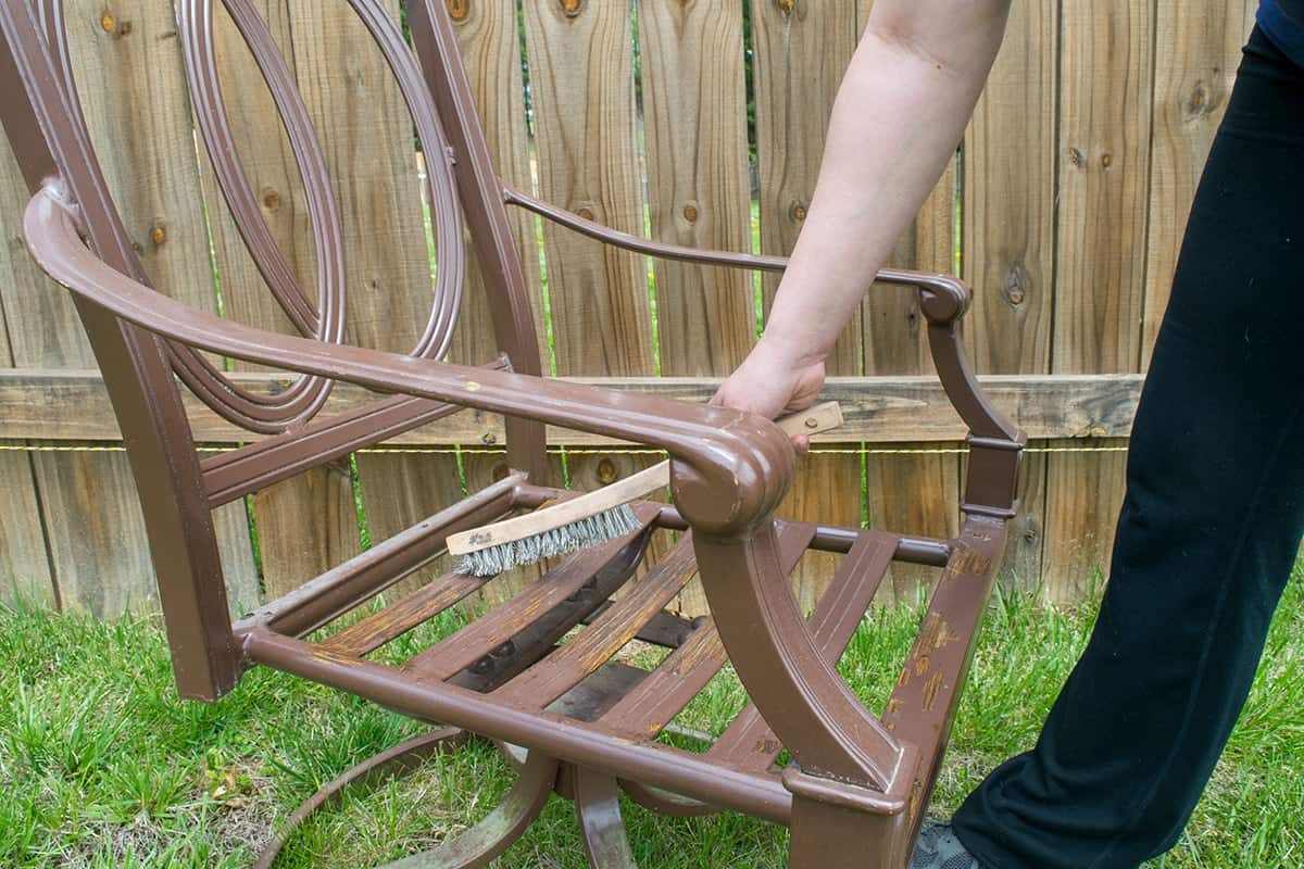 Removing old paint and rust from patio chair using a wire brush.