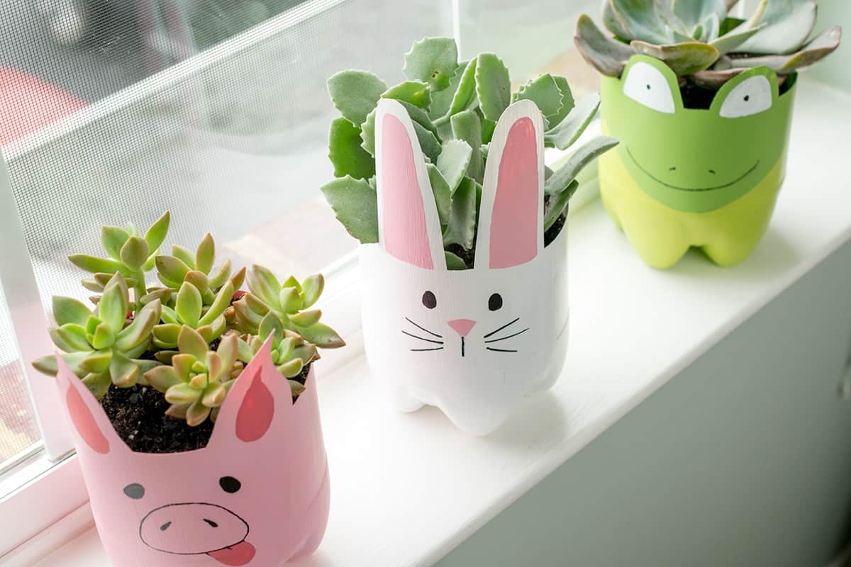 Animal themed soda bottle painted planter crafts with succulents on a white window sill.