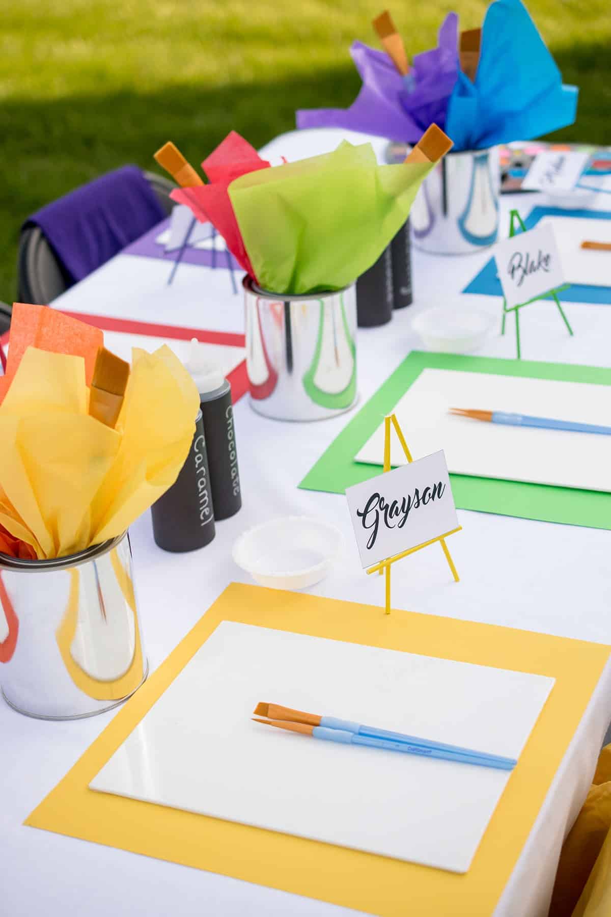 Recycled paint cans with rainbow tissue paper and paint brushes as centerpieces for kid's paint party 