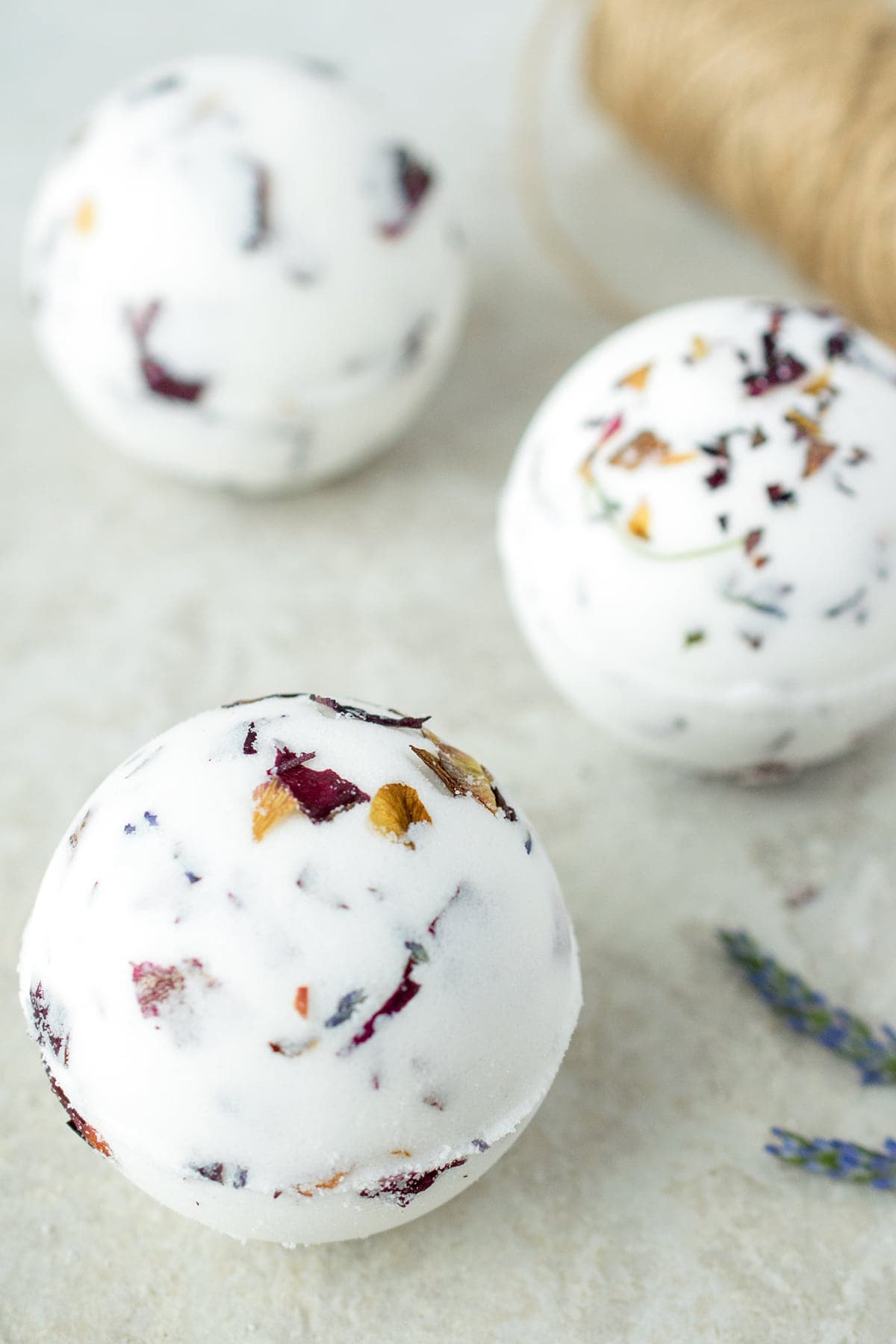 Spherical white lavender bath bombs with rose petal flakes presented with spool of twine