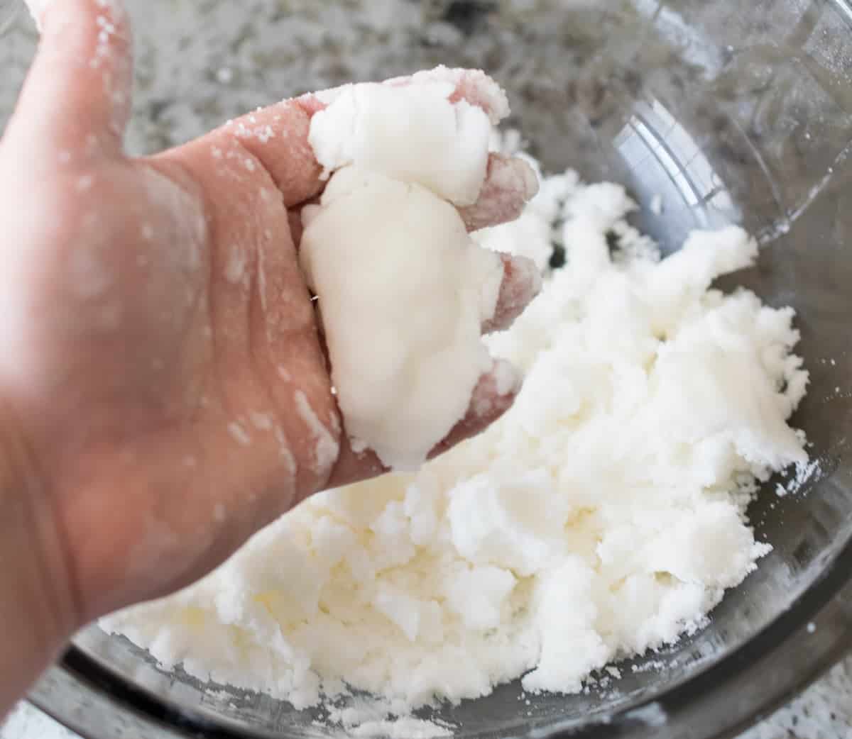 Hand mixing white base for bath bomb mixture in glass bowl