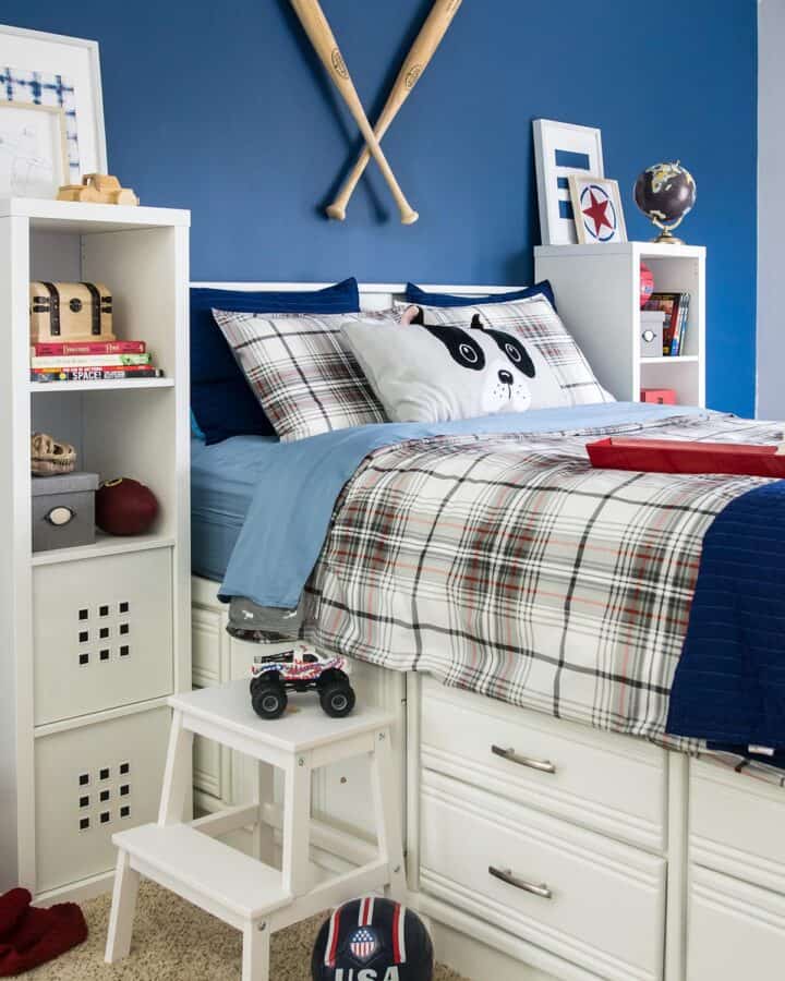 Blue boy's bedroom color scheme with white furniture, tall bed with drawers, blue wall, and baseball bats hanging as art.