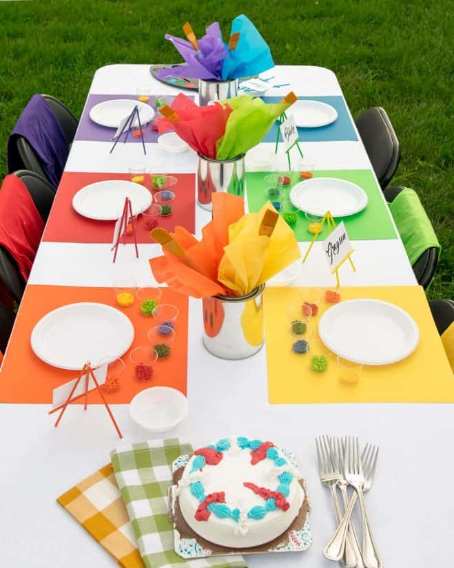 Art party table overhead with place settings, plates, paint and colorful placemats.