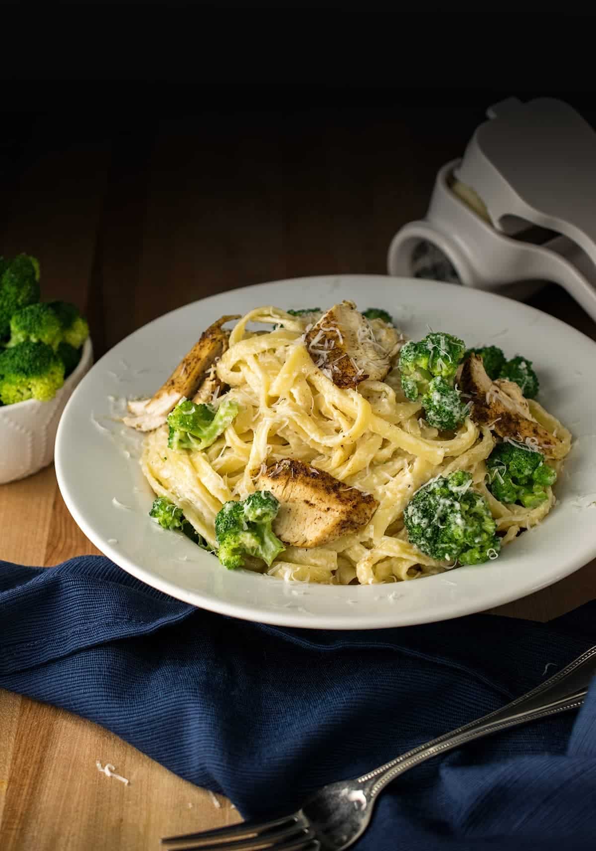 Alfredo pasta with broccoli and cut up blackened chicken in a white bowl.