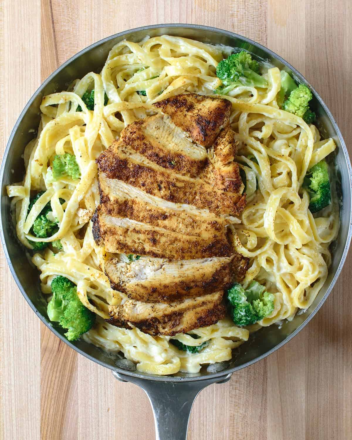 Easy Cajun Chicken Alfredo pasta with homemade Alfredo sauce with broccoli and shredded parmesan in skillet 