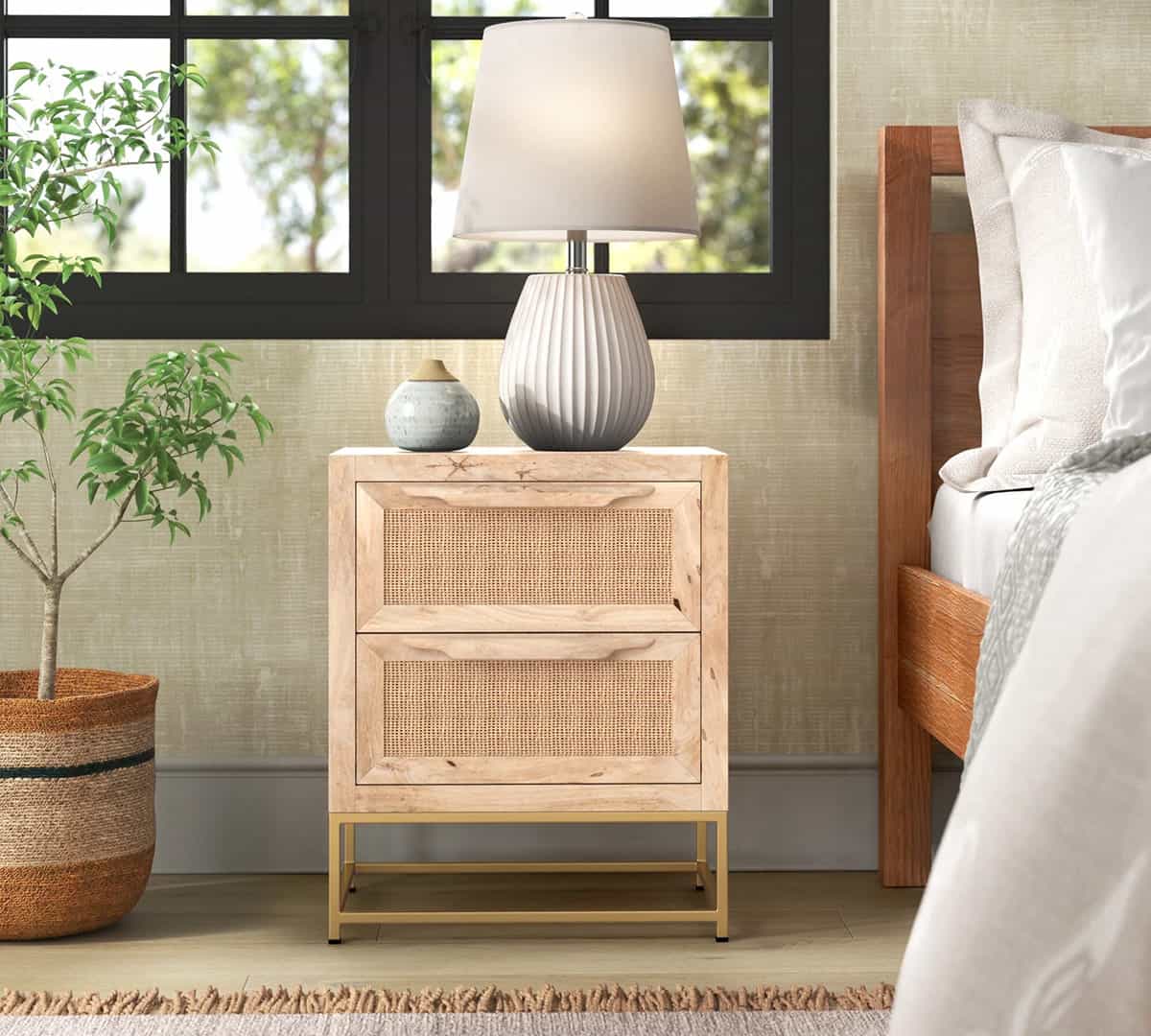 Modern wicker nightstand with gold base adorned with small clay pot and white resin lamp with shade in airy bedroom setting.