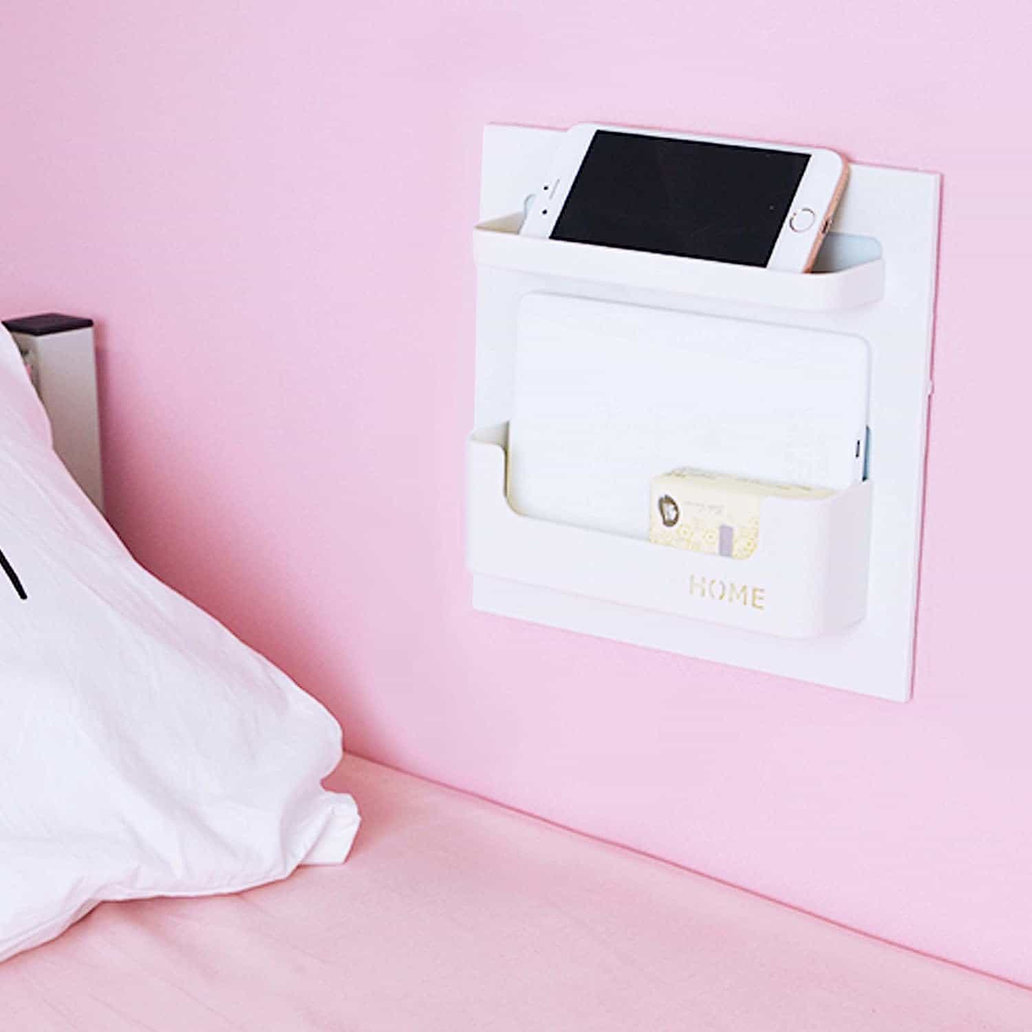 White wall mounted bedside shelf with deep lower pocket containing iPad and shallow top shelf holding iPhone. 