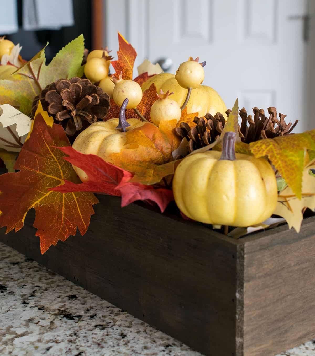 Fall inspired centerpiece on breakfast bar with small pumpkins, pinecones, and artificial autumn leaves.  