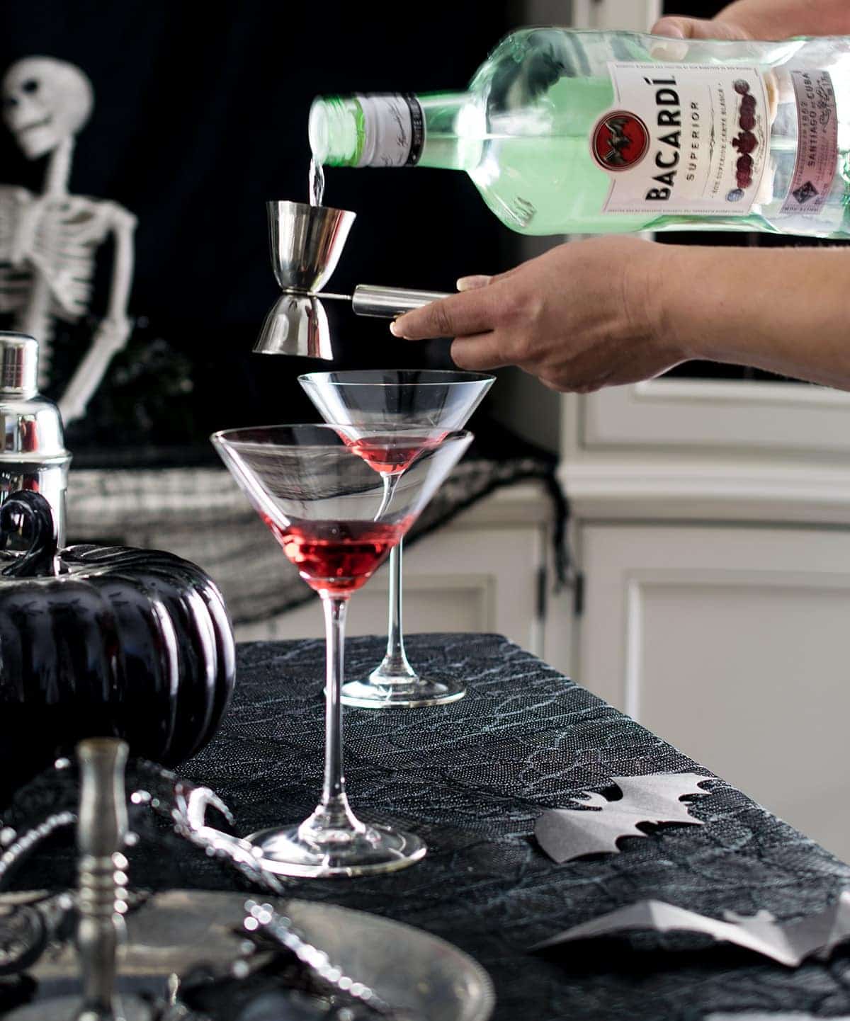 Making a layered cocktail by pouring rum in  jigger over grenadine in a martini glass.
