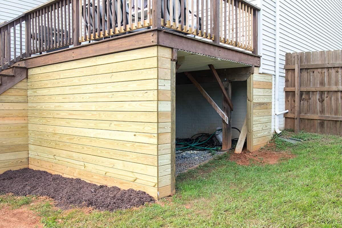 Raised deck with storage shed underneath and enclosed with decking boards. 