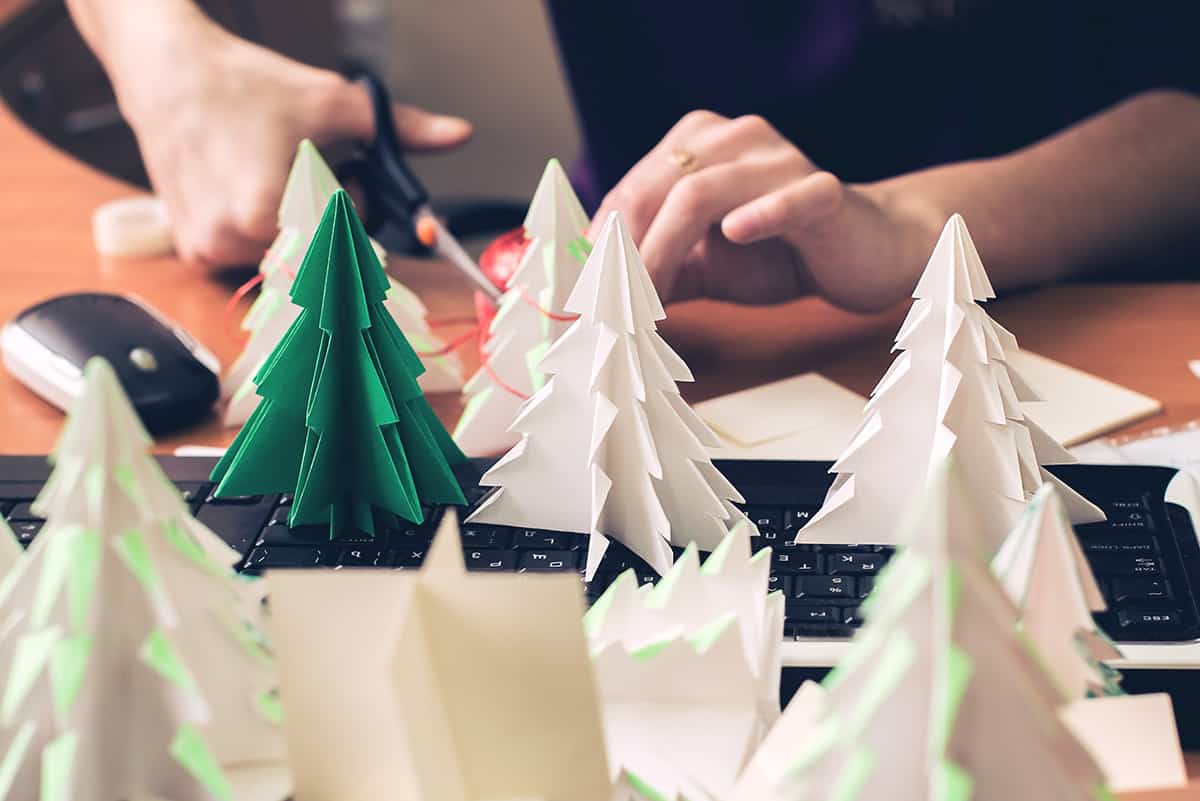 Woman cutting paper trees and folding them into origami Christmas Trees.