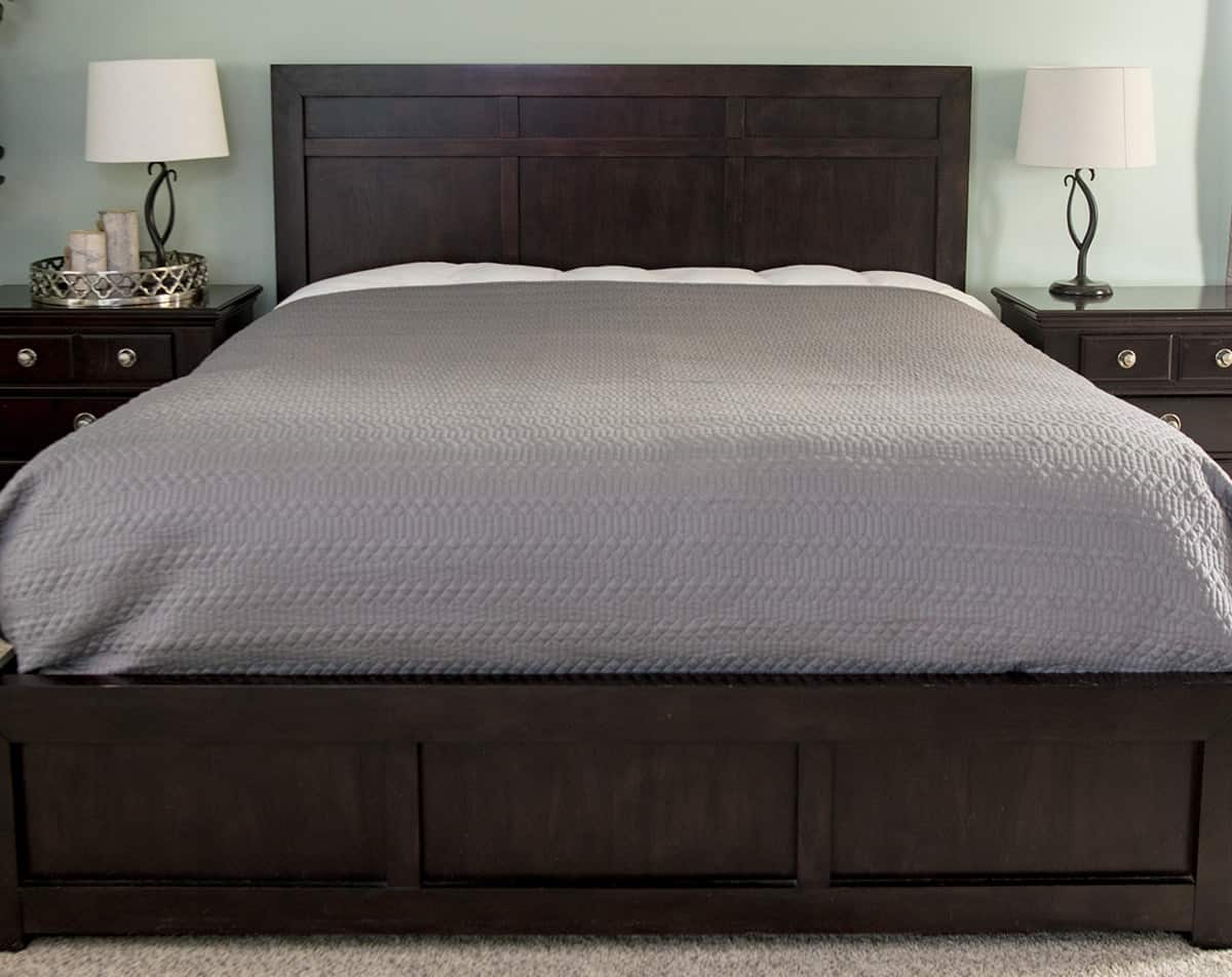 Master bed with duvet and gray textured quilt neatly in place.