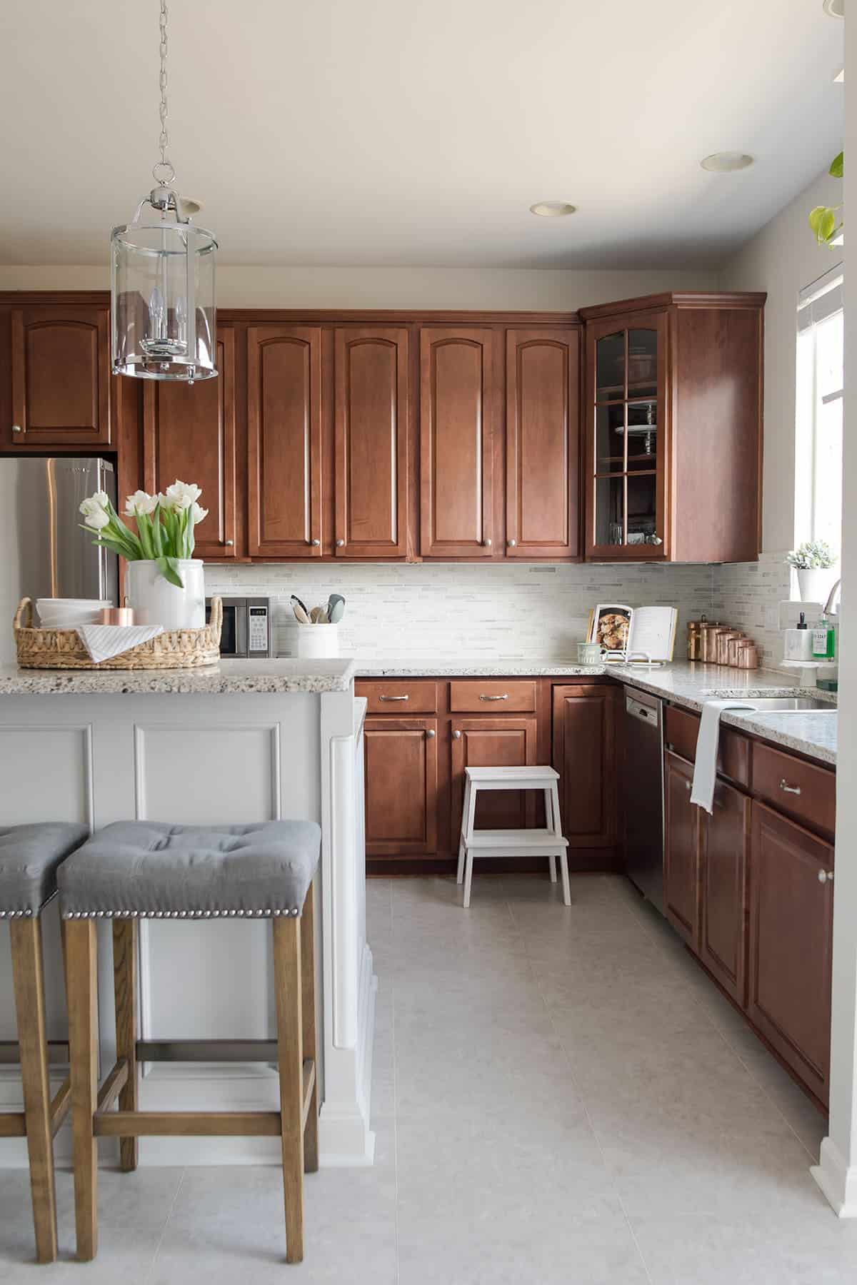 Modern Traditional Kitchen with Wood Cabinets and gray island, light marble countertops, pendant lights, luxury vinyl floor, stainless still appliances, and copper accents. 