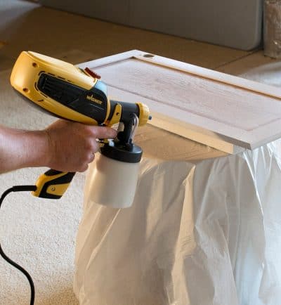 A paint sprayer being used to paint a cabinet door white.