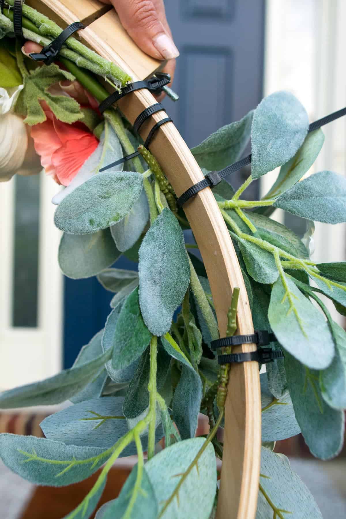 Attaching the greenery and flowers to the hoop base with zip ties.