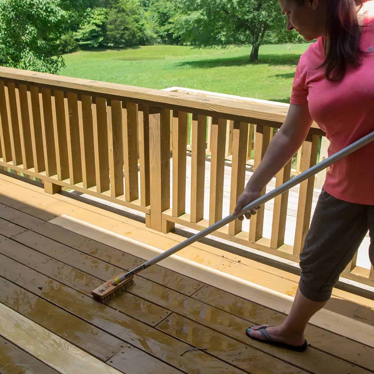 Brushing peeling stain off pressure washed deck with long handled bristle broom.