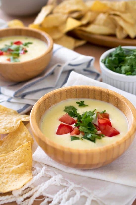 Mexican cheese dip in a small bowl garnished with tomatoes and cilantro.