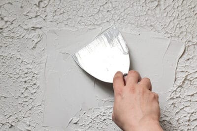 Smoothing out texture on a ceiling with a putty scraper.