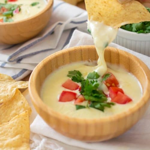 Restaurant style Mexican white Cheese Dip with pico de gallo topping in wooden bowl on dish cloth with chips.