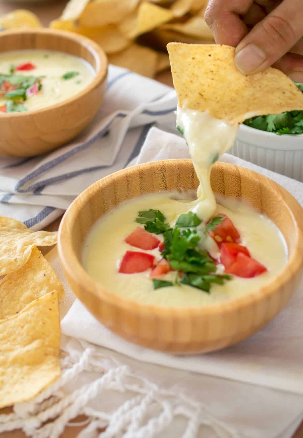 Close up of tortilla chip dipping into queso bowl. Queso topped with pico in wooden bowl container.