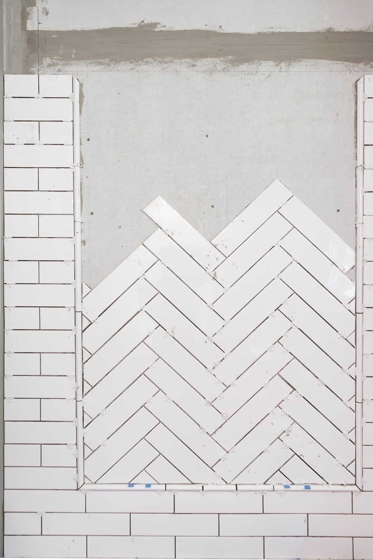 In progress photo of ceramic tile set in herringbone pattern inlay with border surrounded by subway tile shower.