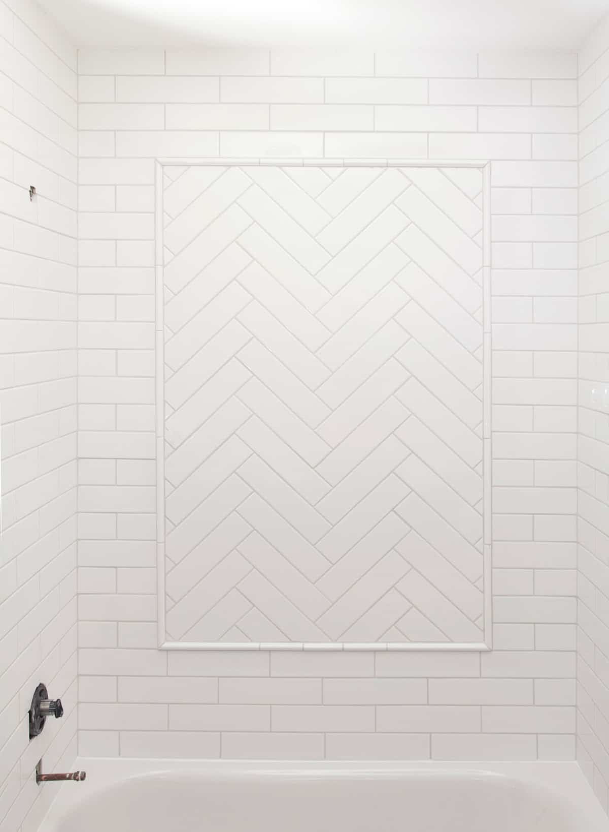 White shower surround with subway tile and herringbone inlay in the center of the wall.