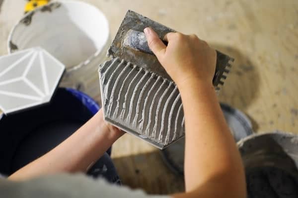 Hands applying mortar to ceramic tile.
