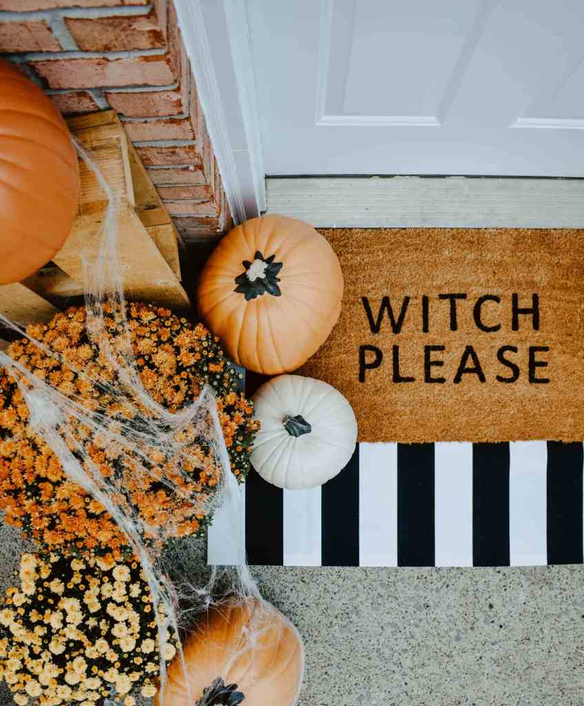 DIY Halloween Doormat laid out with pumpkins and mums around it on a front porch.