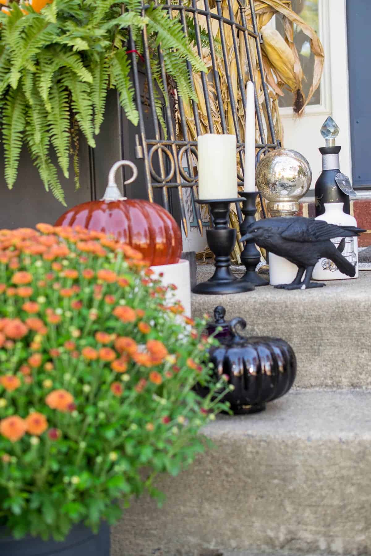 Witch Halloween decor front porch with black crow, potion bottles, glass pumpkins and candlesticks.