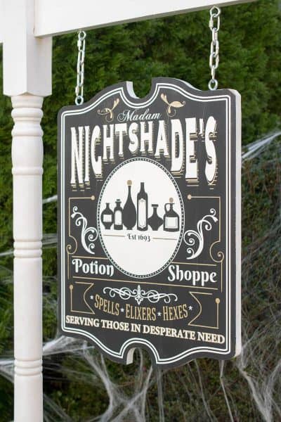 Halloween yard sign with witch's apothecary shop motif hanging on a frame.