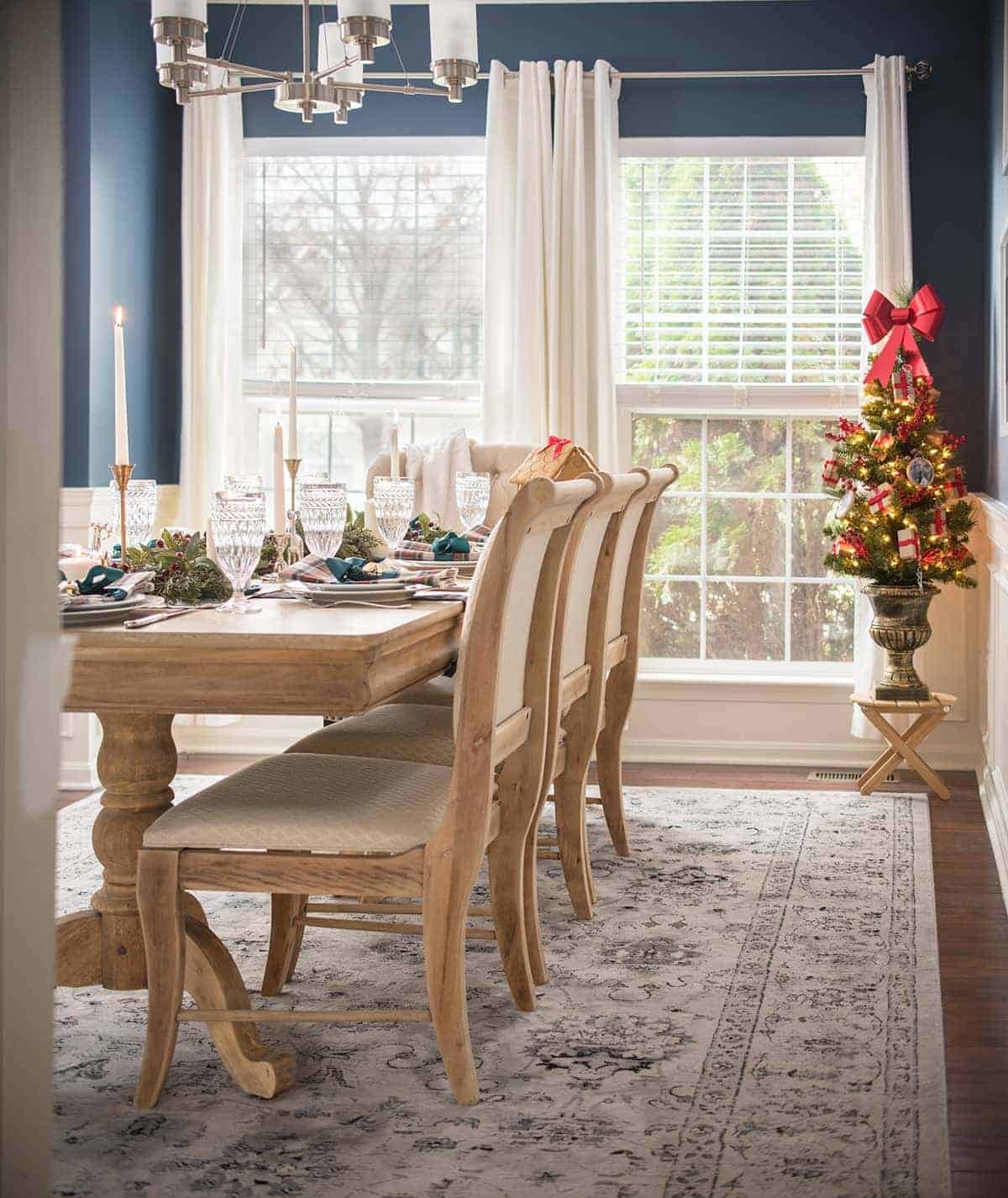 Navy traditional dining room with light wood table and chairs decorated for christmas with tartan and a Christmas tree.