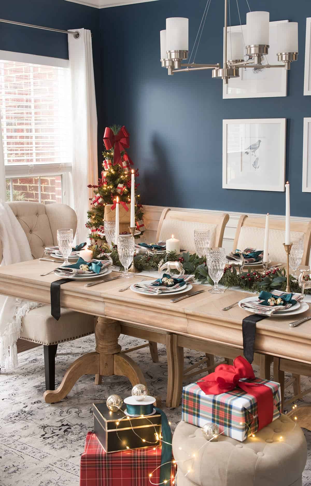 Real wood dining room table. Christmas tartan decor accessorizing dining room.Modern chandelier, modern bird prints, deep cerulean blue walls.