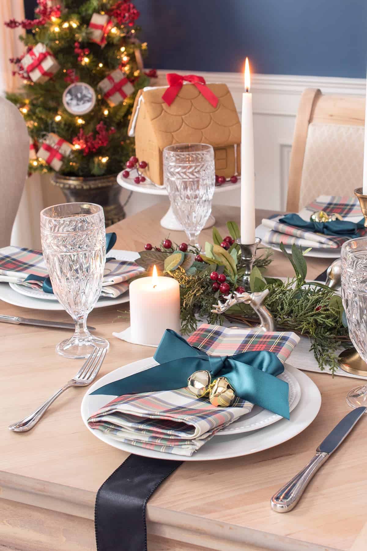 Close up of Christmas dinner table décor and place settings. Gingerbread house on pedestal in background.