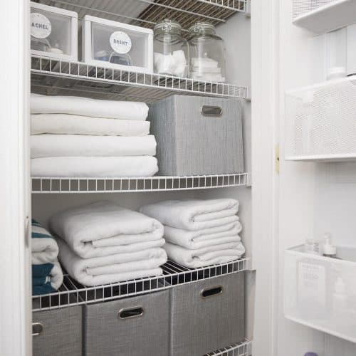 Organized linen closet with white towels and grey bins on wire shelves.