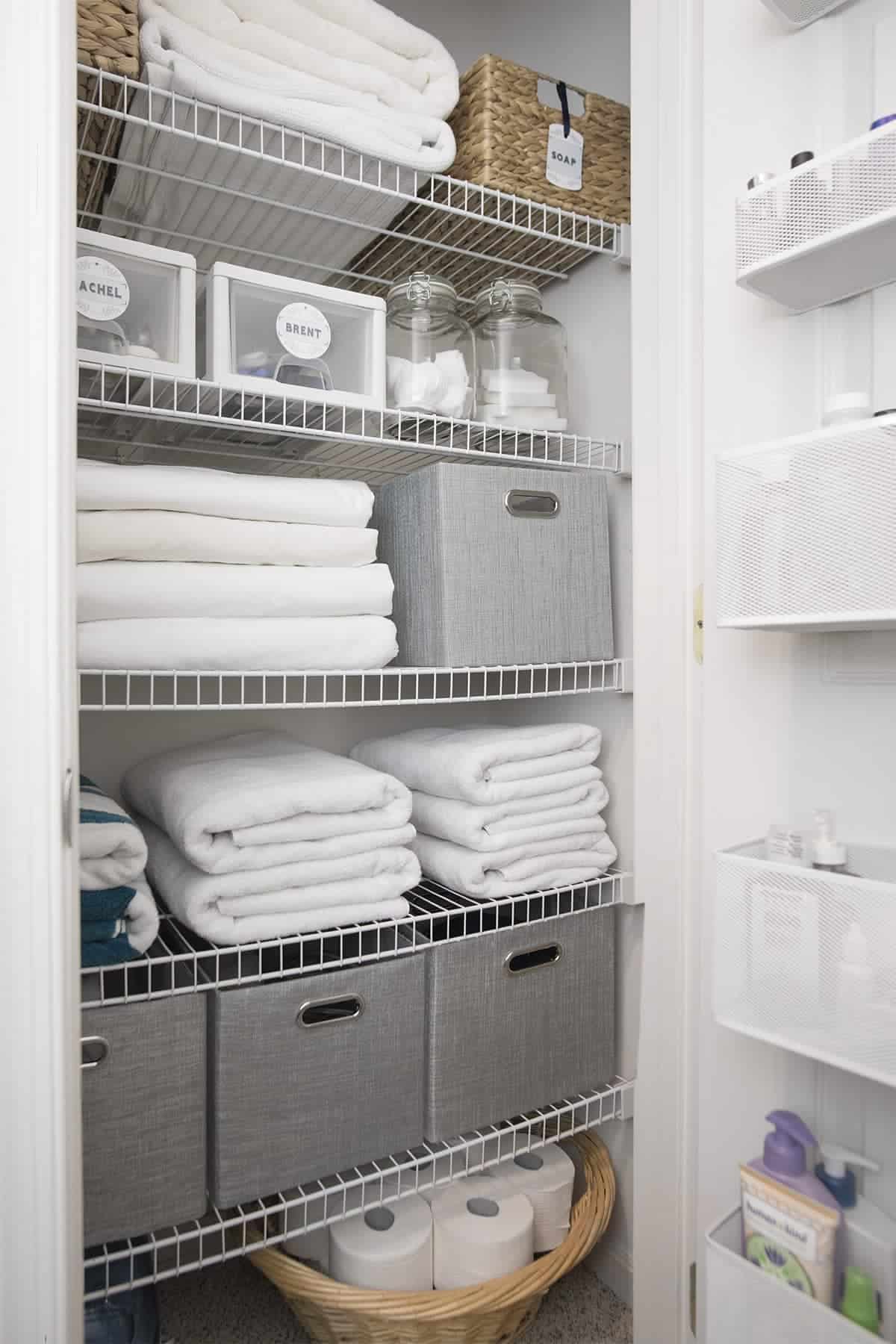 Organized linen closet with bins and baskets and over the door organizer. White & gray hues.