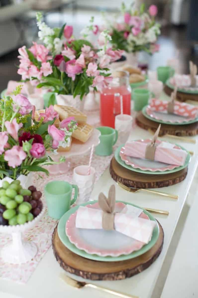 Feminine springtime table setting with green and pink color scheme with row of flower centerpieces.