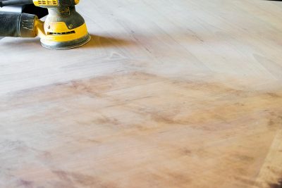 Electric sander removing remaining stain from surface of stripped table.