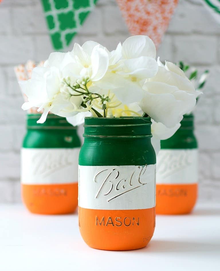 Three mason jars painted orange, green, and white for the Ireland flag decoration filled with delicate white flowers.