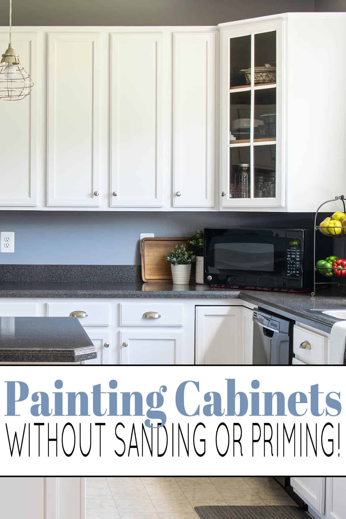 Traditional kitchen with white painted kitchen cabinet with glass door corner cabinet, dark gray countertops, with black microwave, fruit stand, and potted plants. 