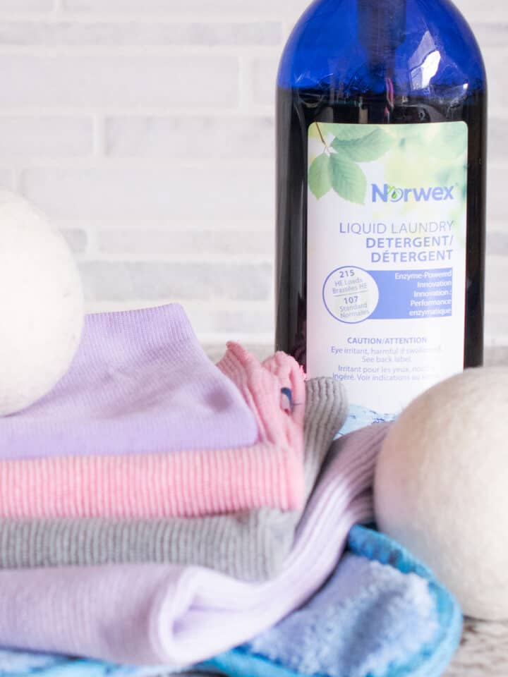 Norwex Enviro Cloth and Window Cloth and two Norwex cleaning balls, solution in background.