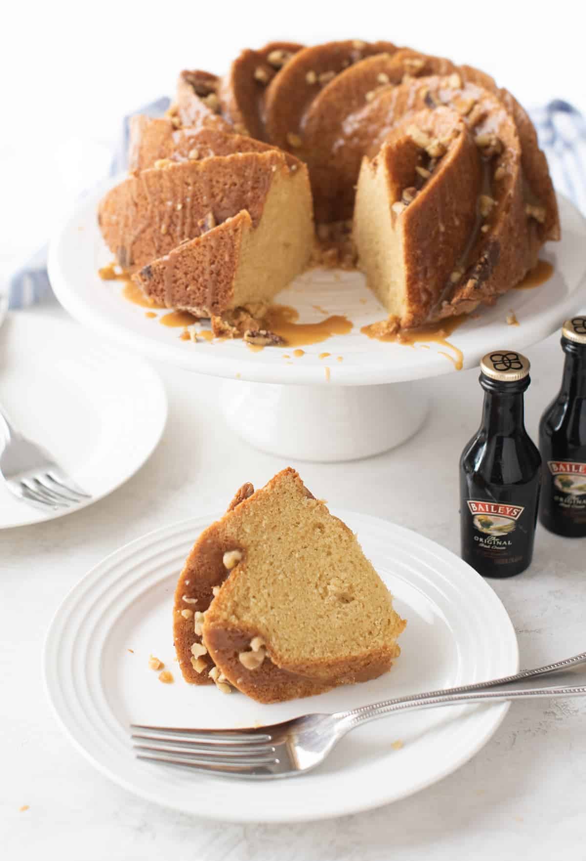 Bailey's Irish Creme Cake perched on white cake stand with one slice removed. 